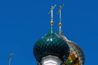 Golden and green domes with crosses of the Russian Orthodox Church against the blue sky